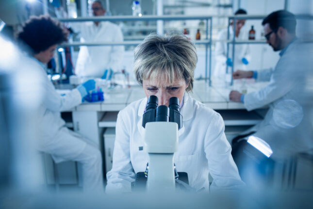 A scientist in a lab analyzes cells through a microscope, illustrating the complexity of understanding CAR-T