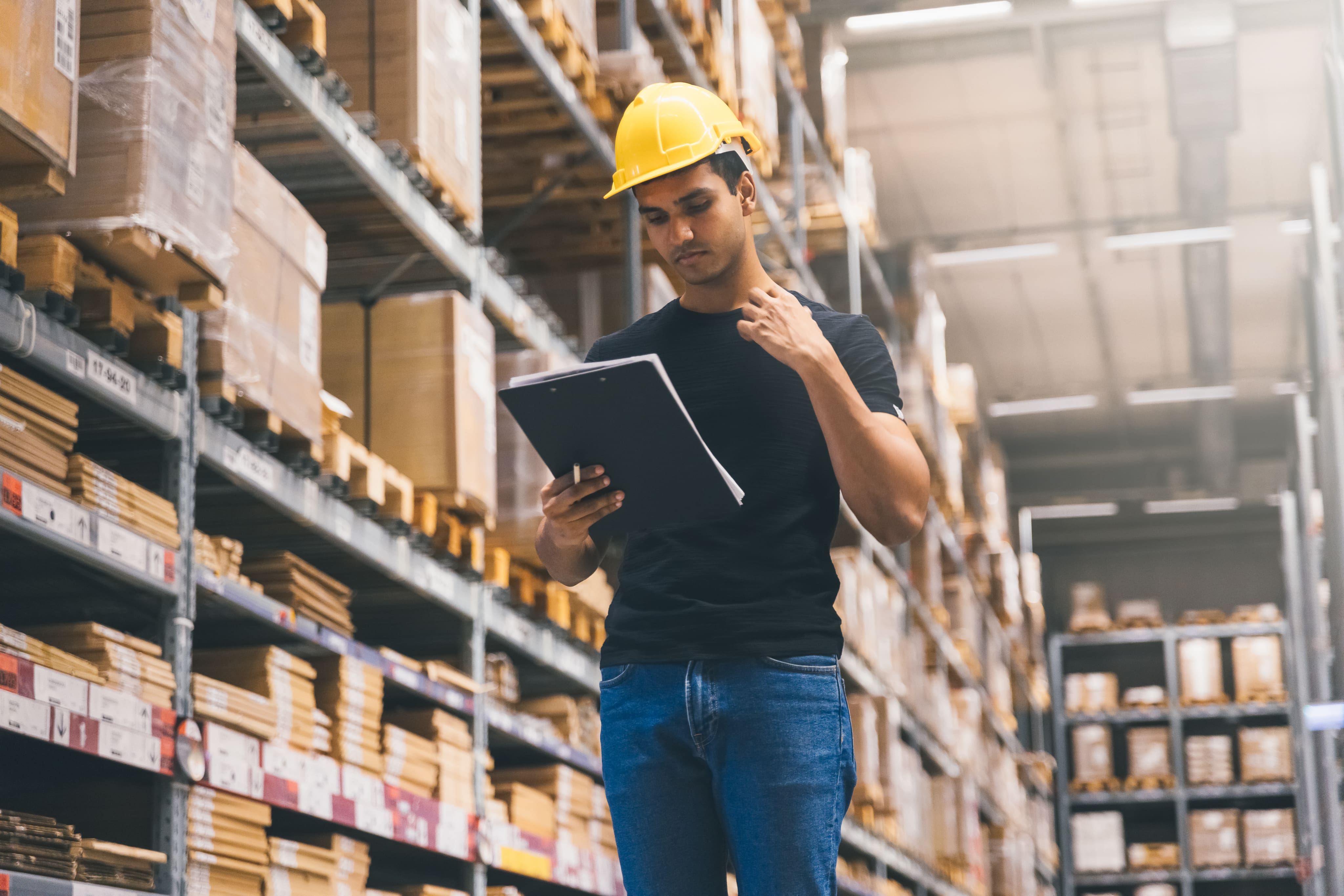 Man in a hardhat looking at a file in a warehouse