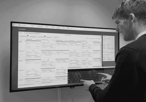 A man interacts with the Binocs schedule board on a large touchscreen display, illustrating one way that Binocs can make lab digitalization work for you