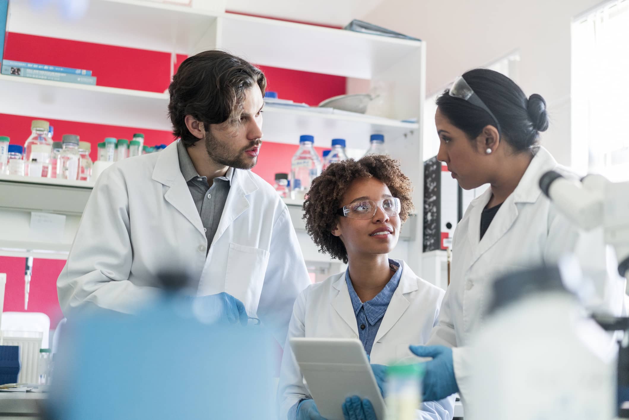 Scientists in conversation over digital tablet in lab. Perhaps they are discussing how much better their QC outcomes are now they are integrated with the Supply chain thanks to Binocs