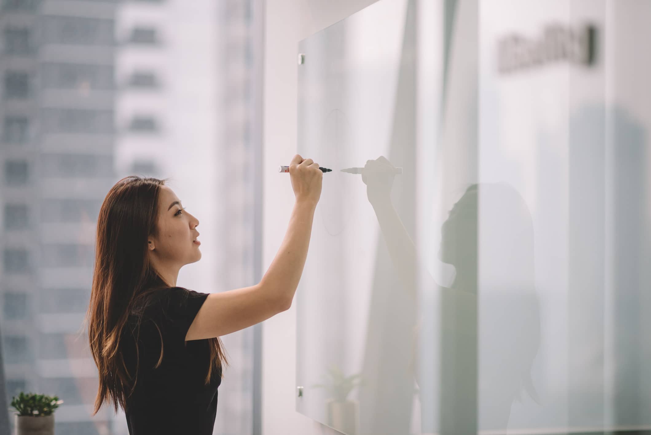 Chinese female writing on white board with her marker pen during conference meeting in office conference room