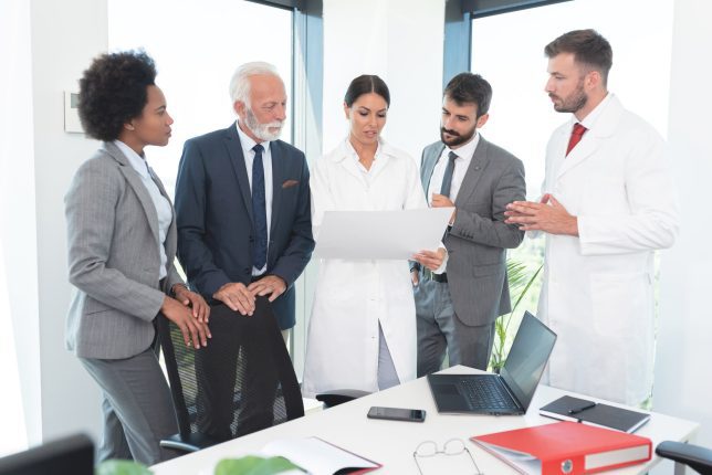 Business people with medical workers analyzing document at office, perhaps to determine the right laboratory resource planning software.