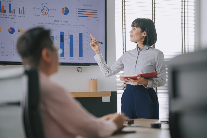 Woman presents to her colleague in conference room with television screen presentation