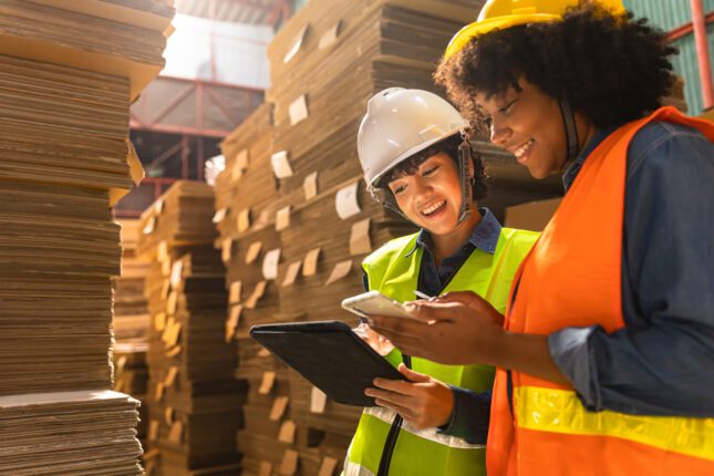 Two warehouse workers discussing over a tablet and cell phone