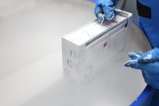 Doctor in hazmat suit working with container with embryonal cells in liquid nitrogen