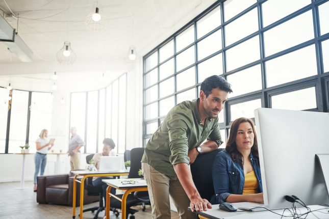 Shot of a male designer assisting his colleague at her desk