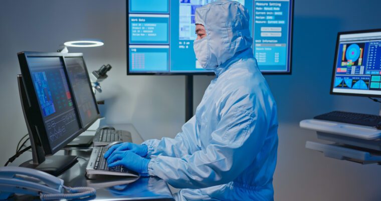 A lab technician wearing sterile coveralls works at a computer terminal, illustrating how building IT infrastructure for CGT requires a dedicated strategy