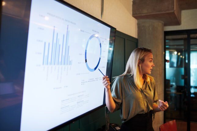 One young businesswoman making a presentation speech, download this free tool to estimate the potential return on investing in a digital lab scheduling system