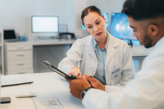 Laboratory staff in white coats discuss data displayed on a tablet device, perhaps looking at 1 of the 4 Quality Control KPIs discussed in this blog post