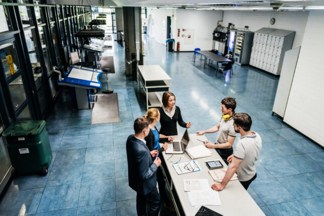 A meeting between a group of engineers at a table on a printing factory floor.