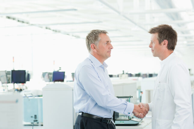 Scientists shaking hands in laboratory, representing the handshake integration that increases QC involvement in E2E planning