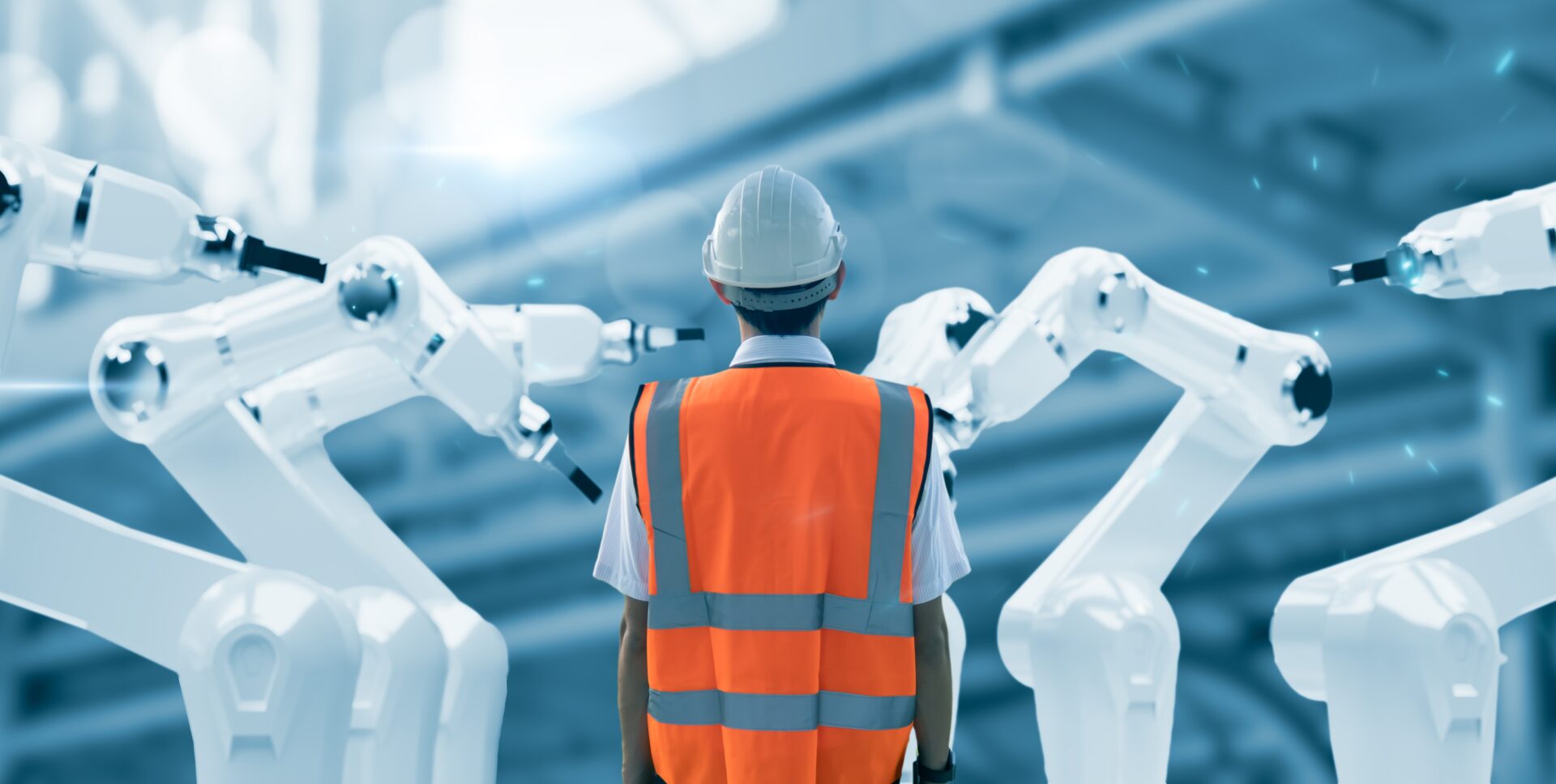 Worker in hard hat stands among robotic arms.