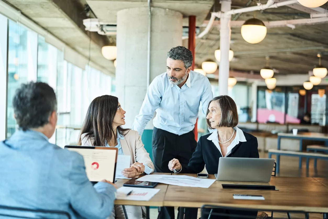 Mature businessman talking with team sitting at table in coworking office. Group of mature business professionals having meeting in office.