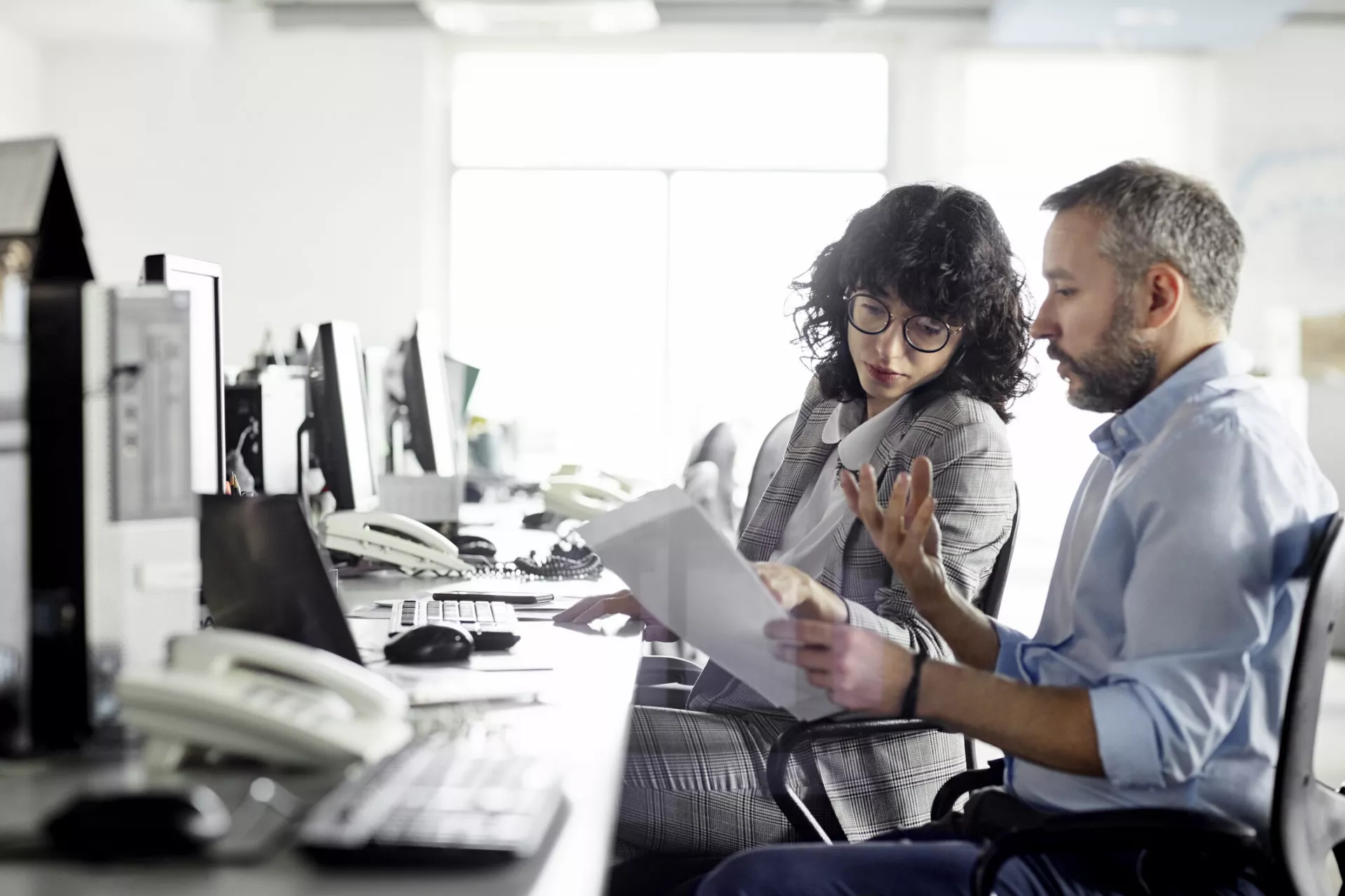 Confident businessman planning strategy with businesswoman. Colleagues are discussing over document at coworking office. They are at desk during meeting.