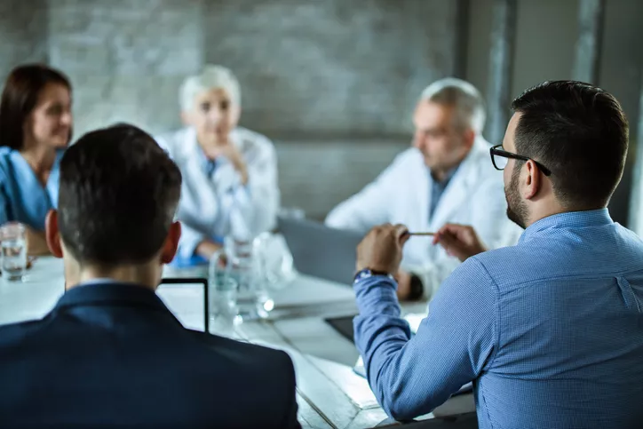 Rear view of businessmen having a business meeting with team of doctors at doctor's office. Focus is on man on the right.
