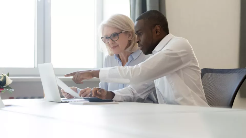 African american employee pointing at laptop discussing paperwork with colleague working together focused on computer task, black business employee helping giving online presentation to client