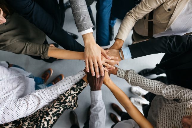 AI enabled laboratory scheduling to help lab teams work efficiently. The image shows a group of colleagues standing in a circle and stacking hands in a team affirmation.
