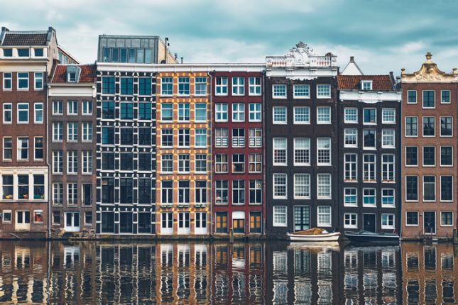 Row of typical houses and boat on Amsterdam canal Damrak with reflection