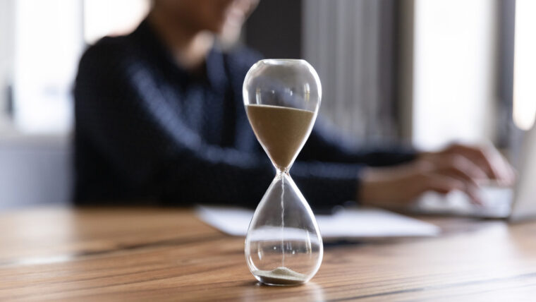 Hourglass counts the time as employee works at desk, maybe measuring how a digital twin saves time